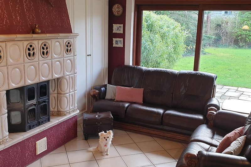 Wohnzimmer mit brauner Couch, Pflanze, Hund, Uhr und Fenster. Gemütliche Einrichtung.