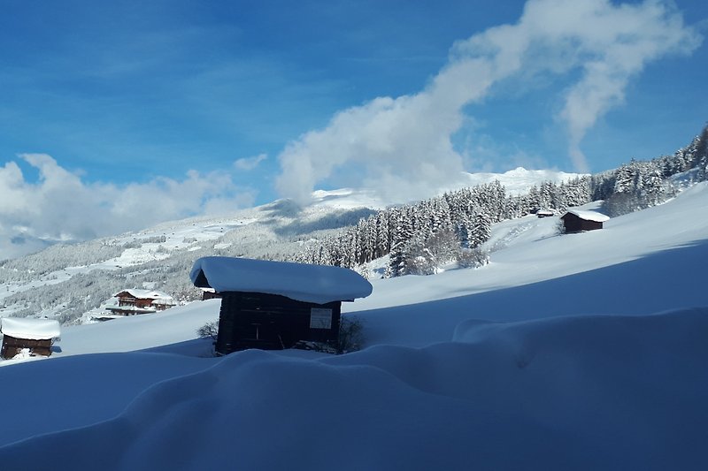 Ein winterliches Bergpanorama mit schneebedeckten Gipfeln und einem gemütlichen Haus.