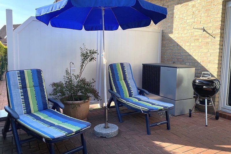 Gemütliche Terrasse mit Sonnenschirm und bequemen Gartenmöbeln sowie Weber-Holzkohlegrill.