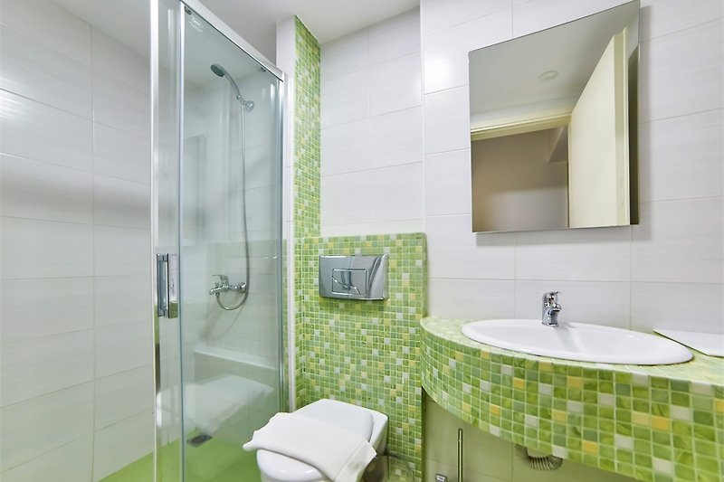 Badezimmer mit Spiegel, Waschbecken, Dusche und grünen Pflanzen.