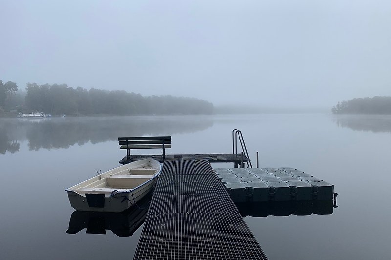 Ruhiger See mit Nebel, Boot und Holzsteg.