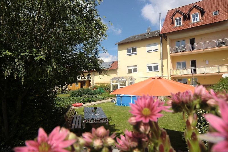 Blühender Garten mit Haus und blauen Himmel.