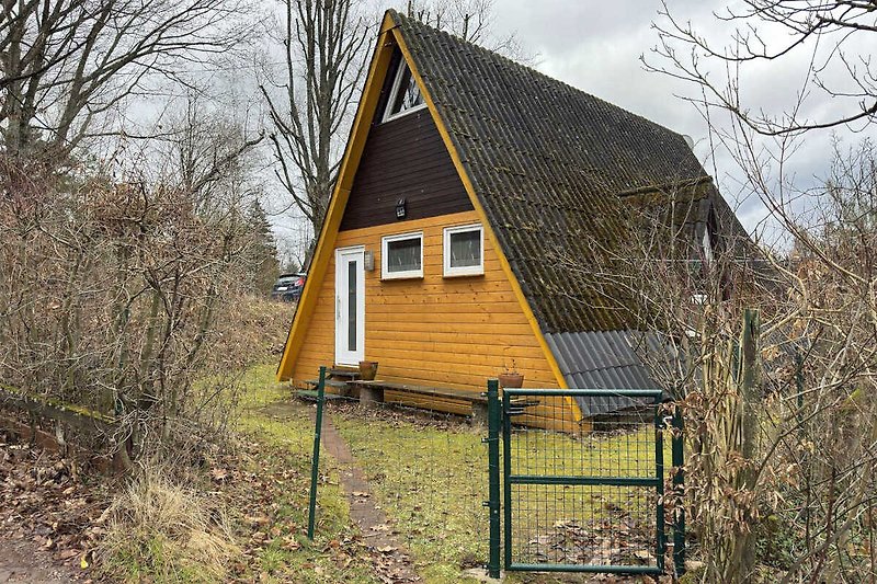 Holzhütte mit Schuppen und Garten im Hintergrund.