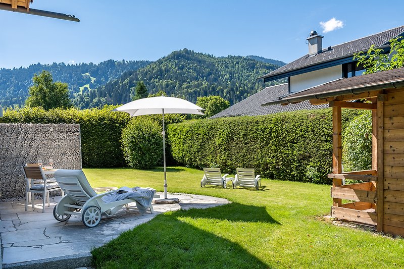 Ferienhaus mit Bergblick, Gartenmöbeln und grüner Landschaft.
