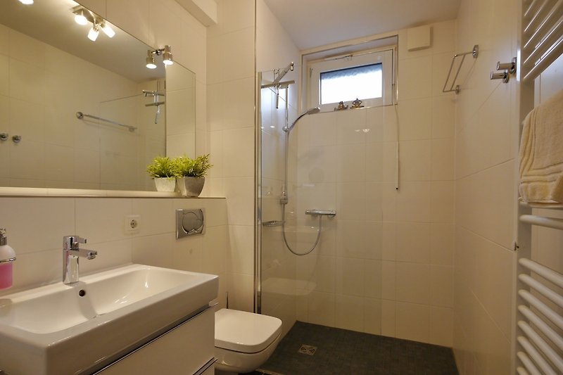 Łazienka z prysznicem z podgrzewana podłogą, oknem, grzejnikiem na ręczniki, suszarką do włosów.
