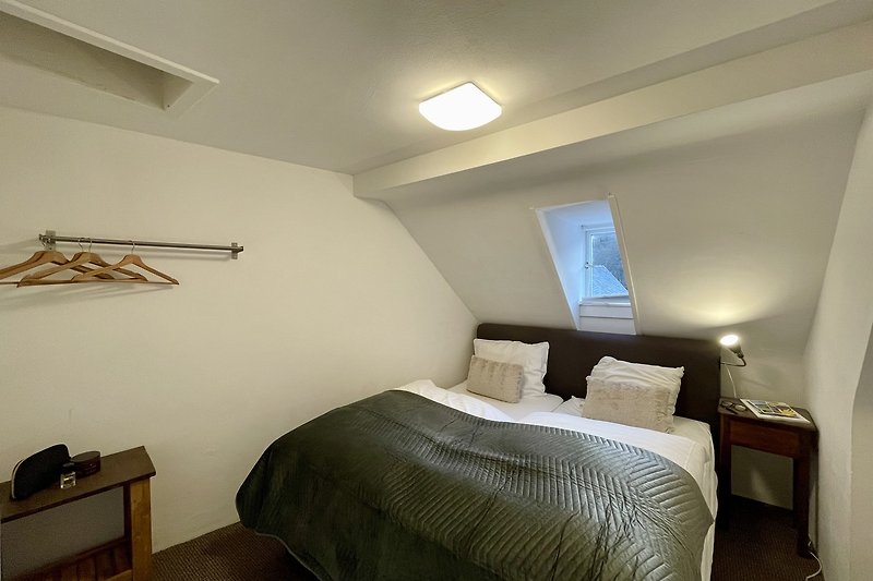 Schlafzimmer mit Holzmöbeln, Bettwäsche und Lampe.