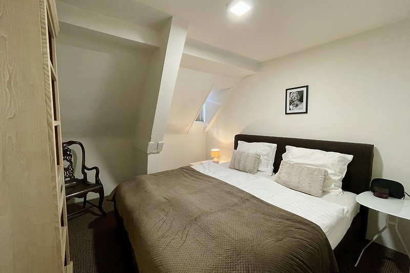 Schlafzimmer mit Holzmöbeln, Bettwäsche und Lampe.