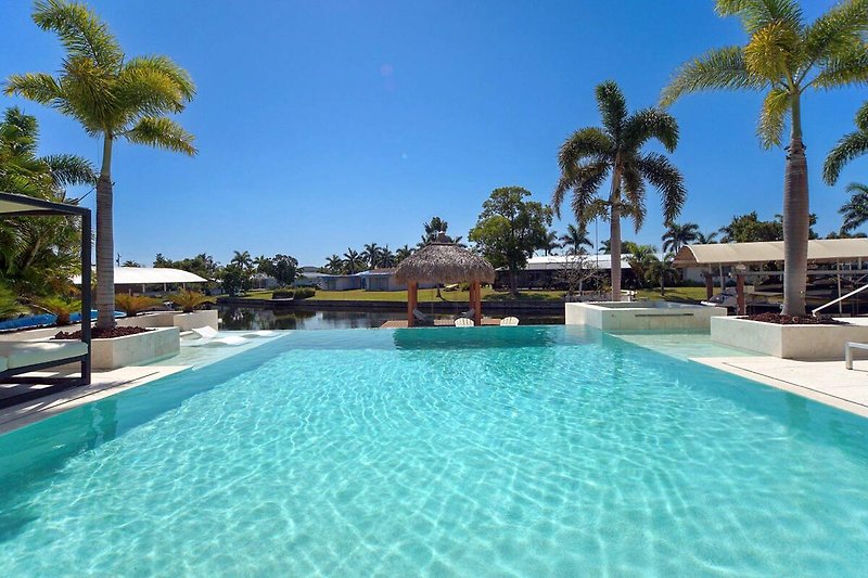 Luxuriöser Poolbereich mit Palmen, Sonnenliegen und azurblauem Wasser.