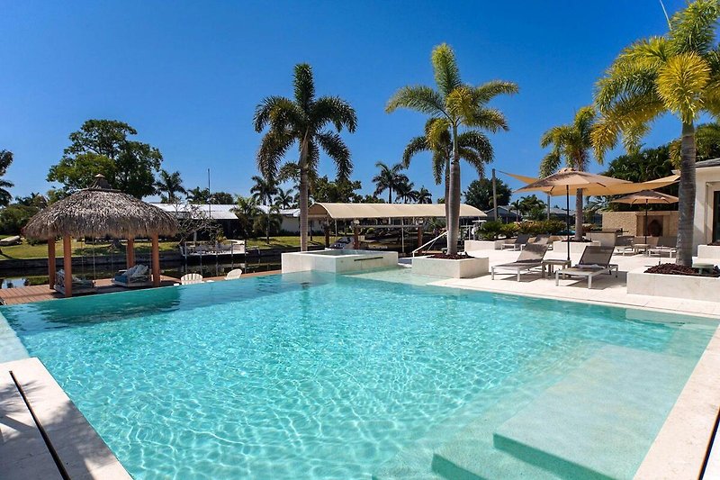 Luxuriöser Poolbereich mit Sonnenschirmen, Palmen und Pool.