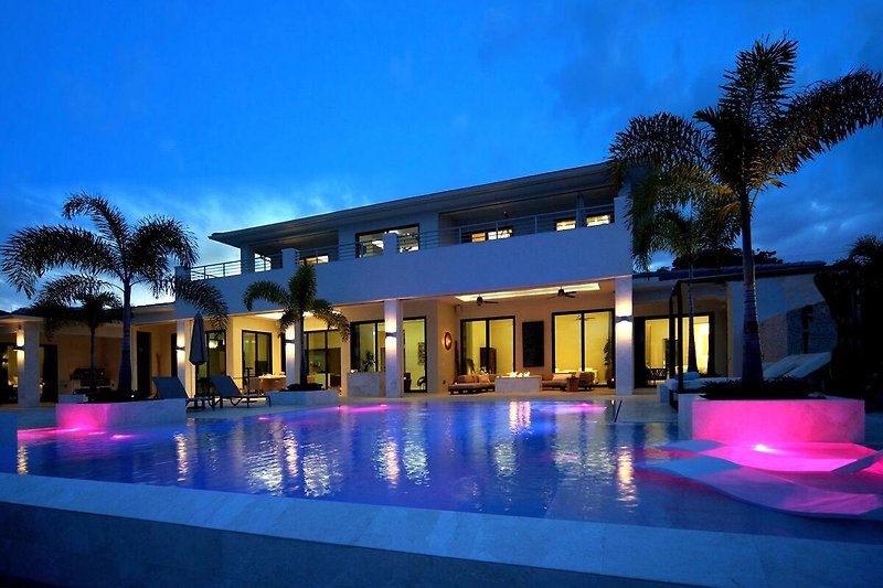 Luxuriöser Poolbereich mit azurblauem Wasser, Palmen und Sonnenschirmen.