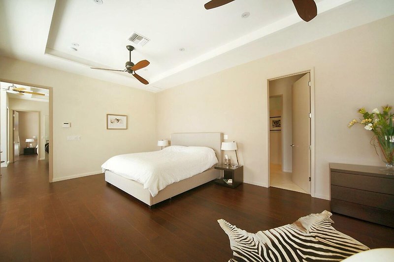Schlafzimmer mit gemütlichem Bett, Holzmöbeln und Deckenventilator.