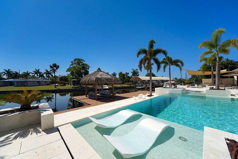 Luxuriöses Resort mit Pool, Palmen und Sonnenliegen.