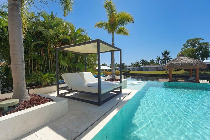 Luxuriöses Resort mit Pool, Palmen und Sonnenliegen.