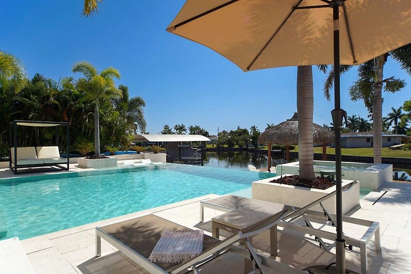 Luxuriöser Poolbereich mit Sonnenschirmen, Palmen und Sonnenliegen.
