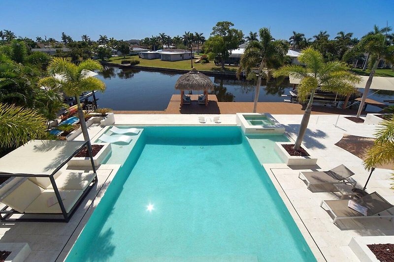 Luxuriöser Poolbereich mit Sonnenliegen, Palmen und azurblauem Wasser.