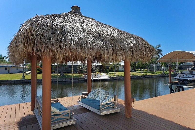 Karibisches Ferienhaus am See mit Boot, Palmen und Sonnenliegen.