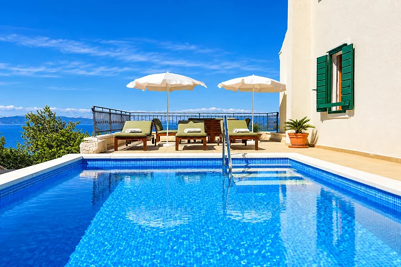 Poolterrasse mit Liegen und blauem Himmel.