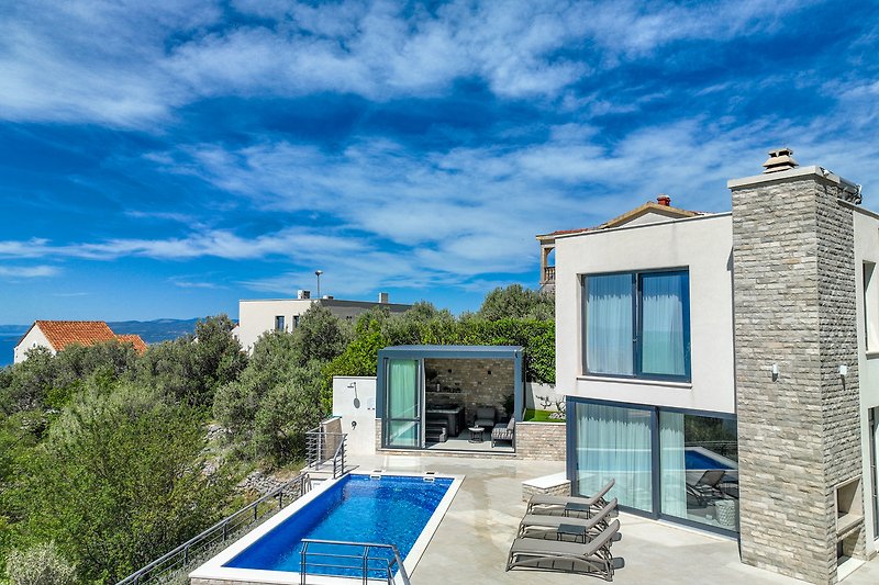 Luxuriöse Villa mit Pool, blauer Himmel und grüner Landschaft.