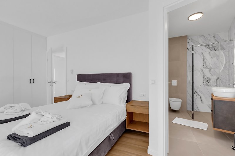 Komfortables Schlafzimmer mit weißem Holzbett und grauen Textilien.