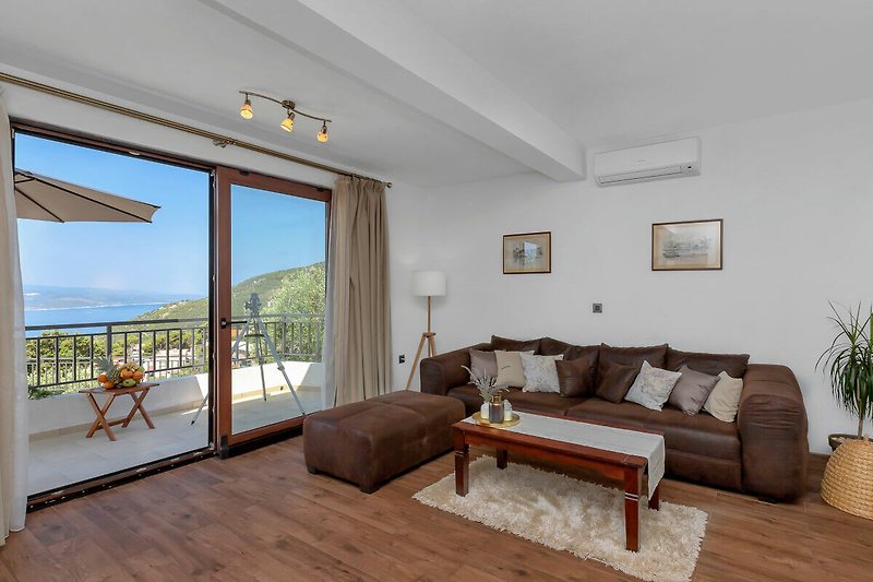 Gemütliches Wohnzimmer mit bequemer Couch, Holzmöbeln und Terrasse mit Meerblick