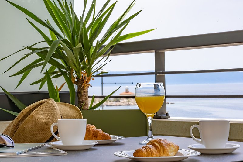 Frühstückstisch mit Geschirr, Pflanzen und Meerblick.