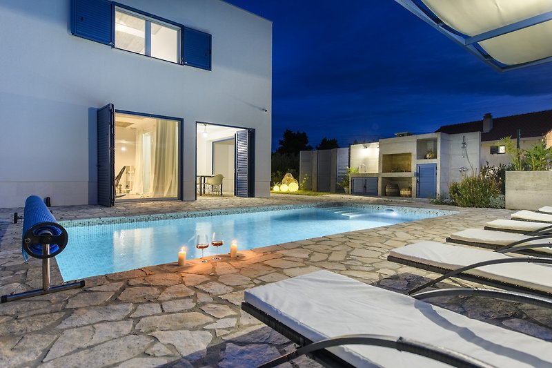 Schwimmbad mit Gebäude, Terrasse, Außenmöbeln und blauem Wasser.