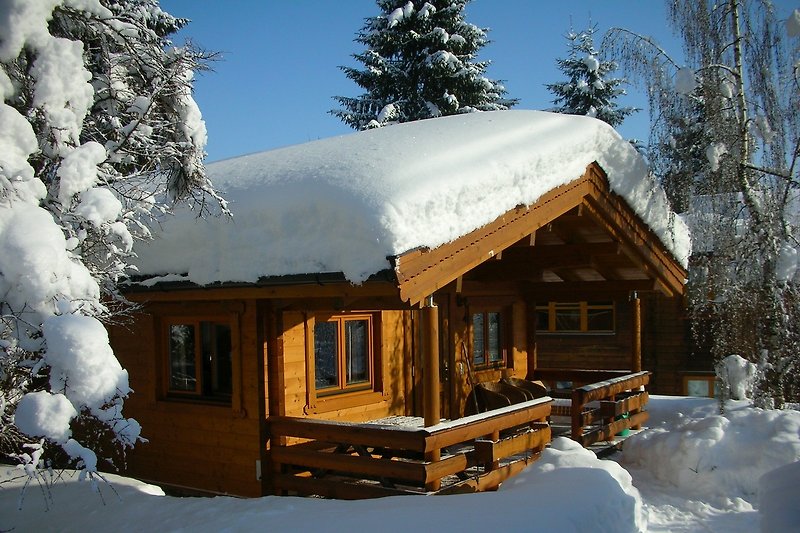 Ein winterliches Holzhaus mit Blick auf die verschneite Landschaft.