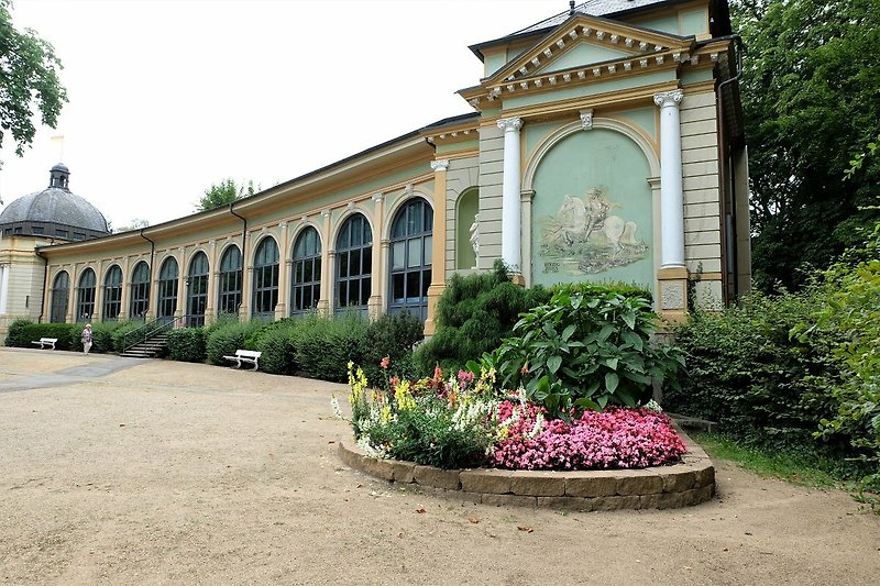 Bad Harzburger Wandelhalle  mit Trinkbrunnen im blühenden Garten und historischer Architektur.