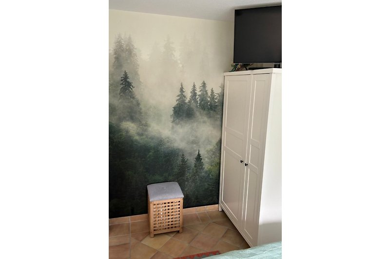 kuscheliges Schlafzimmer mit Fernseher und Wandblick auf Bergtannen im Nebel