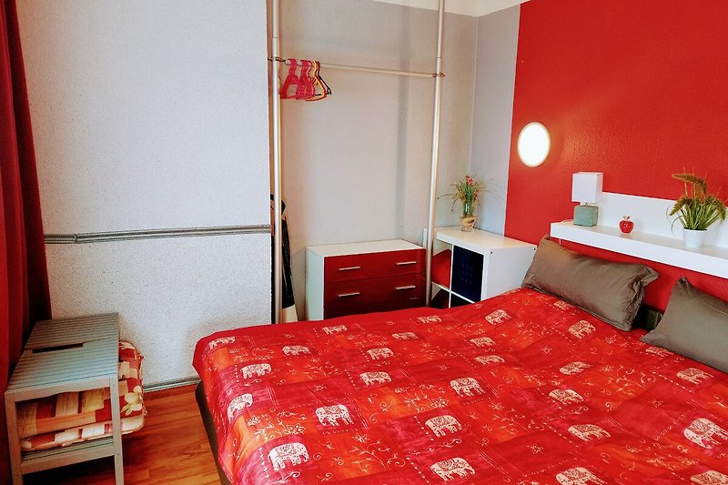 Rotes Bett mit Holzrahmen, Lampenschirm und Blumen - Schlafzimmer-Akzent.