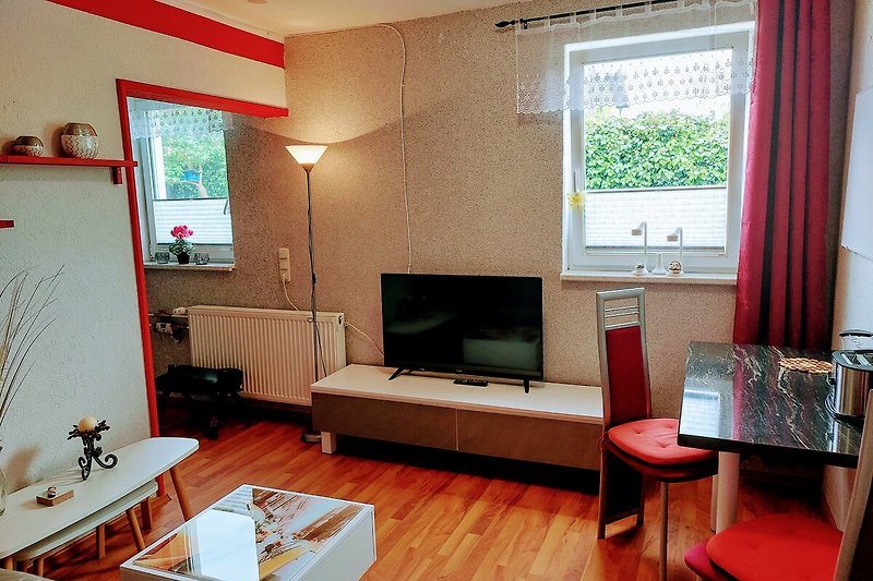 Wohnzimmer mit gemütlicher Couch, Fernseher und Pflanze - entspannte Atmosphäre.