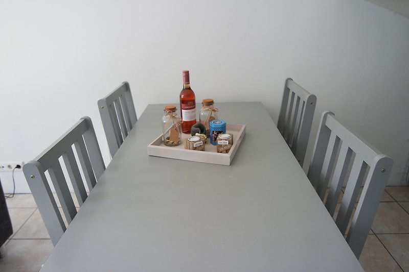 Tisch mit Flasche, Gläsern, Wein und Stühlen.