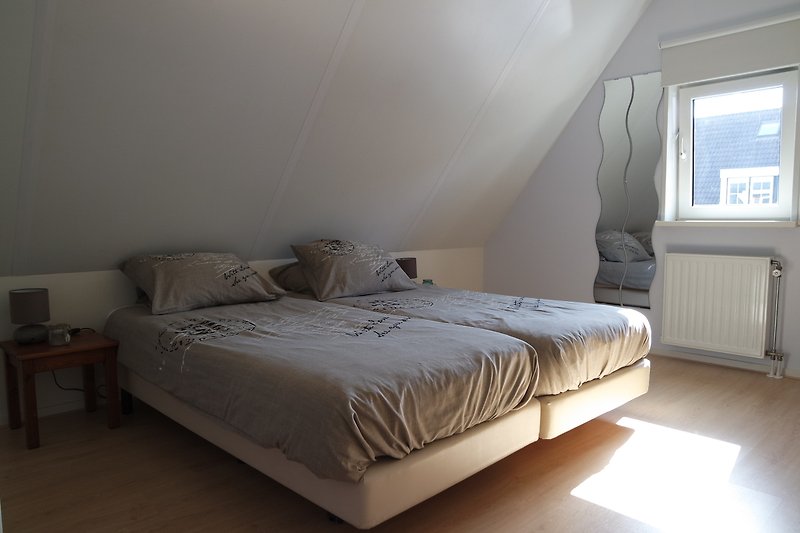 Schlafzimmer mit bequemem Bett, Fenster und Holzbettgestell.