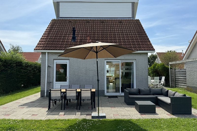 Charmantes Landhaus mit Veranda, Gartenmöbeln und üppigem Grün.