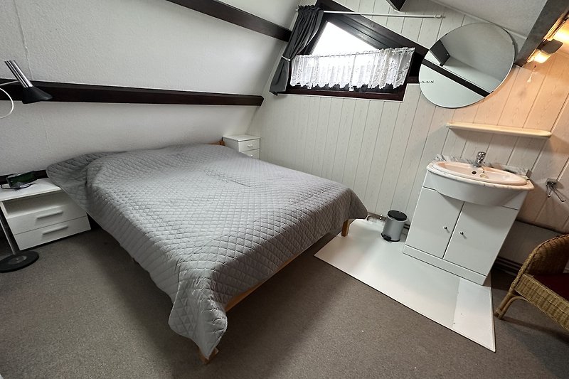 Schlafzimmer mit gemütlichem Bett, Spiegel und Lampen.