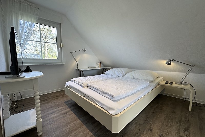 Schlafzimmer mit Holzbett, Bettwäsche und Sash-Fenster.