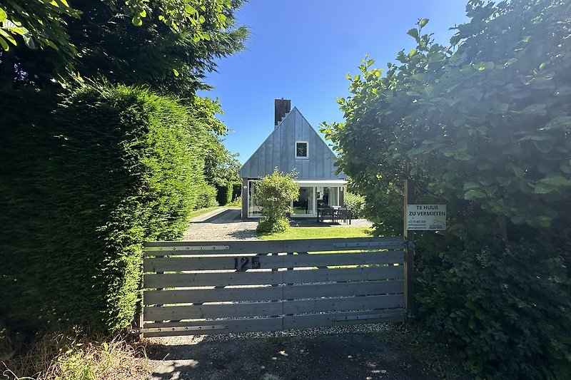 Gemütliches Landhaus mit Garten, Zaun und blühenden Sträuchern.