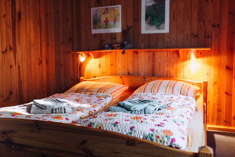Gemütliches Schlafzimmer mit Holzbett, orangenen Kissen und Fensterblick.