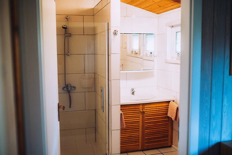Schönes Badezimmer mit Holzboden, Fliesen und Duschtür.