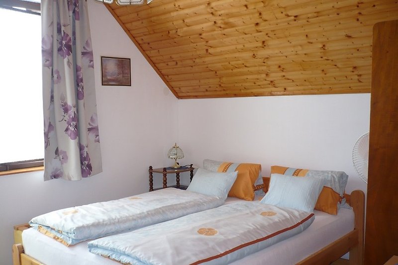 Gemütliches Schlafzimmer mit Holzmöbeln und Fensterbehang.