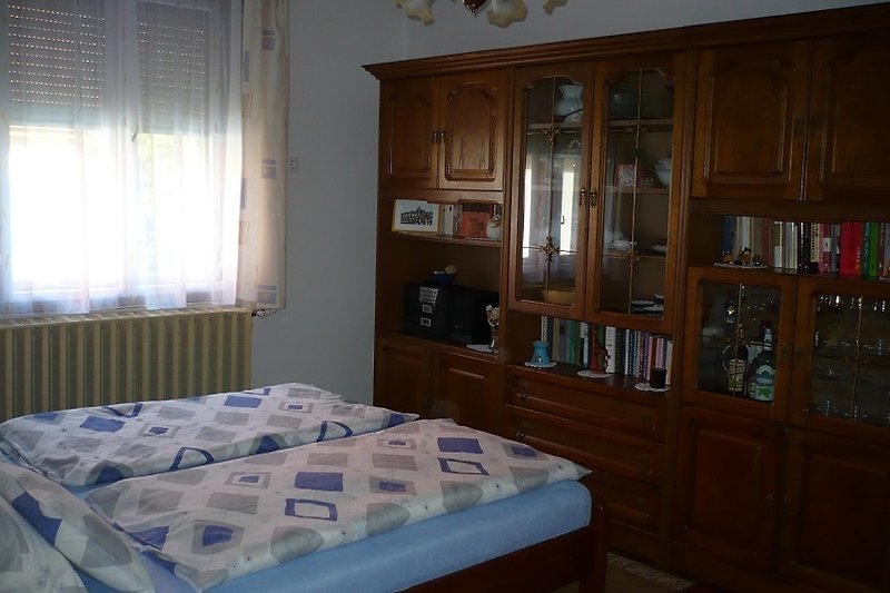 Gemütliches Schlafzimmer mit antikem Holzmöbel und Fensterdekoration.