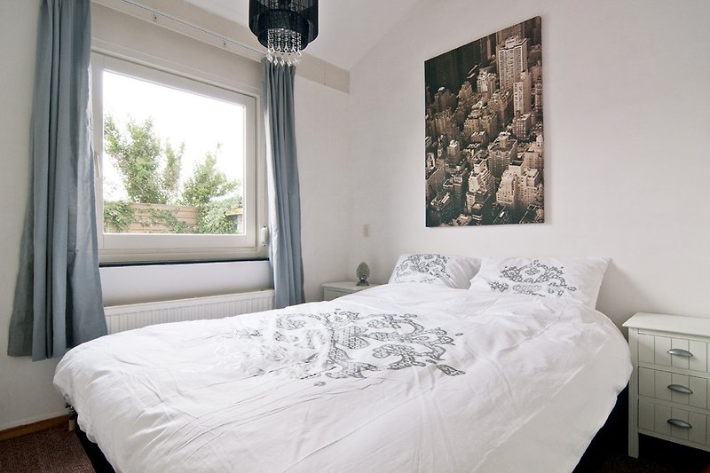 Gemütliches Schlafzimmer mit weißem Bett, Holzmöbeln und grauen Vorhängen.