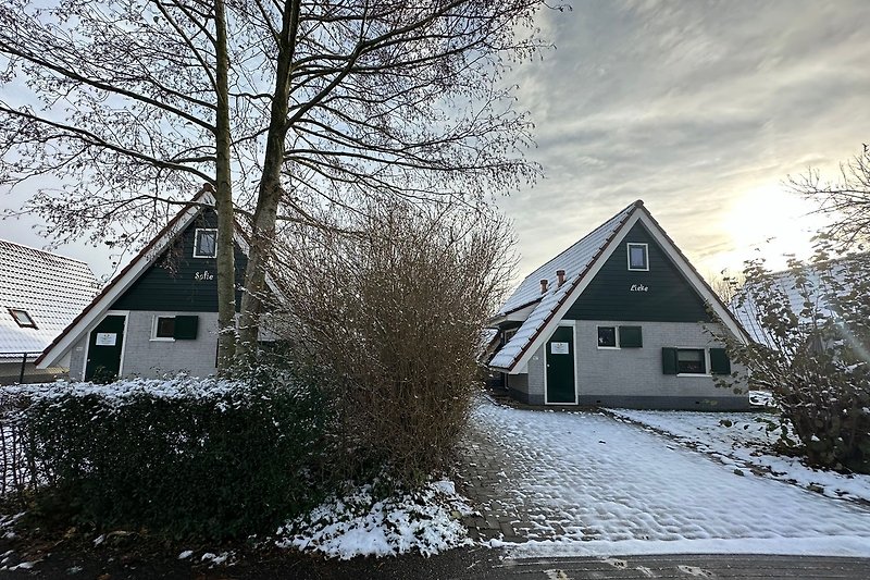 Winterlandschaft mit traditionellem Bauernhaus, Schnee und frostigen Bäumen.