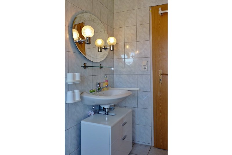 Badezimmer mit Spiegel, Waschbecken und Beleuchtung.