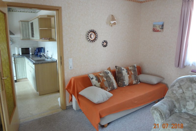 Wohnzimmer mit bequemer Couch, Holzmöbeln, Lampe und Bilderrahmen.