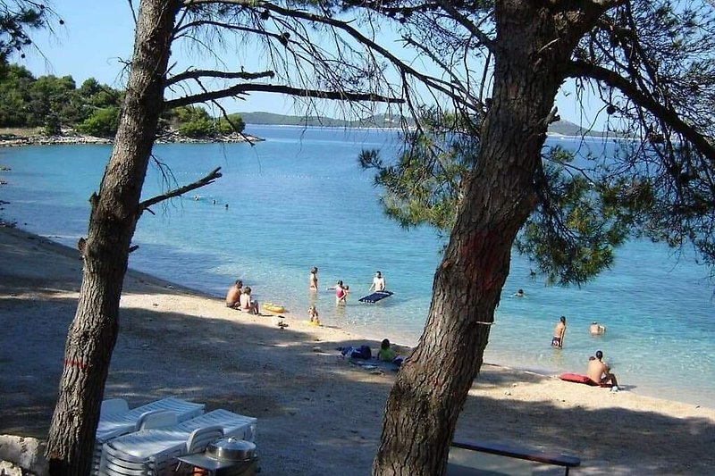 Schöner Strand mit azurblauem Wasser, Menschen und Palmen am Horizont.