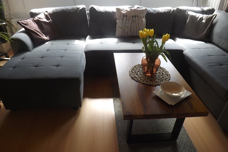 Wohnzimmer mit Holzmöbeln, Blumen und gemütlicher Couch.