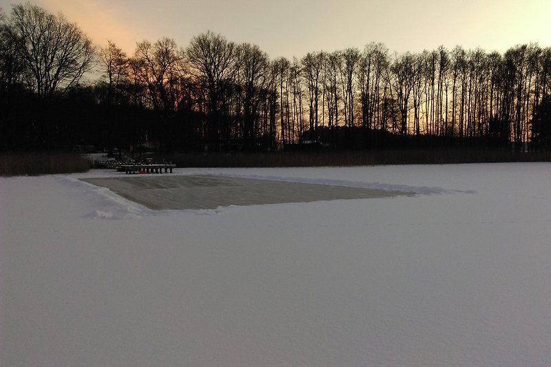 Blick vom zugefrorenen See auf Steg und Haus