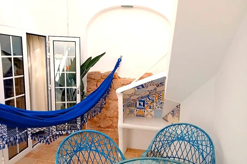 Wicker-Sessel, bunte Kissen und Pflanzen schaffen wohnliches Flair.