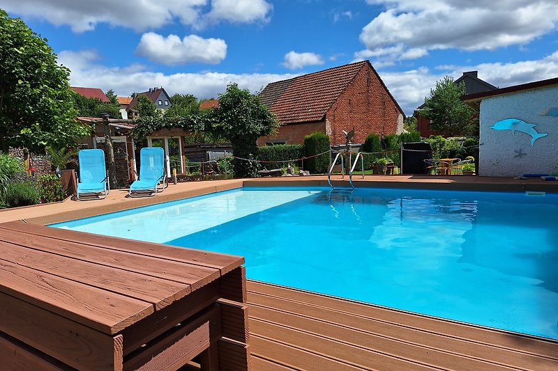 Sonnige Terrasse mit Pool, Palmen und Gartenmöbeln.